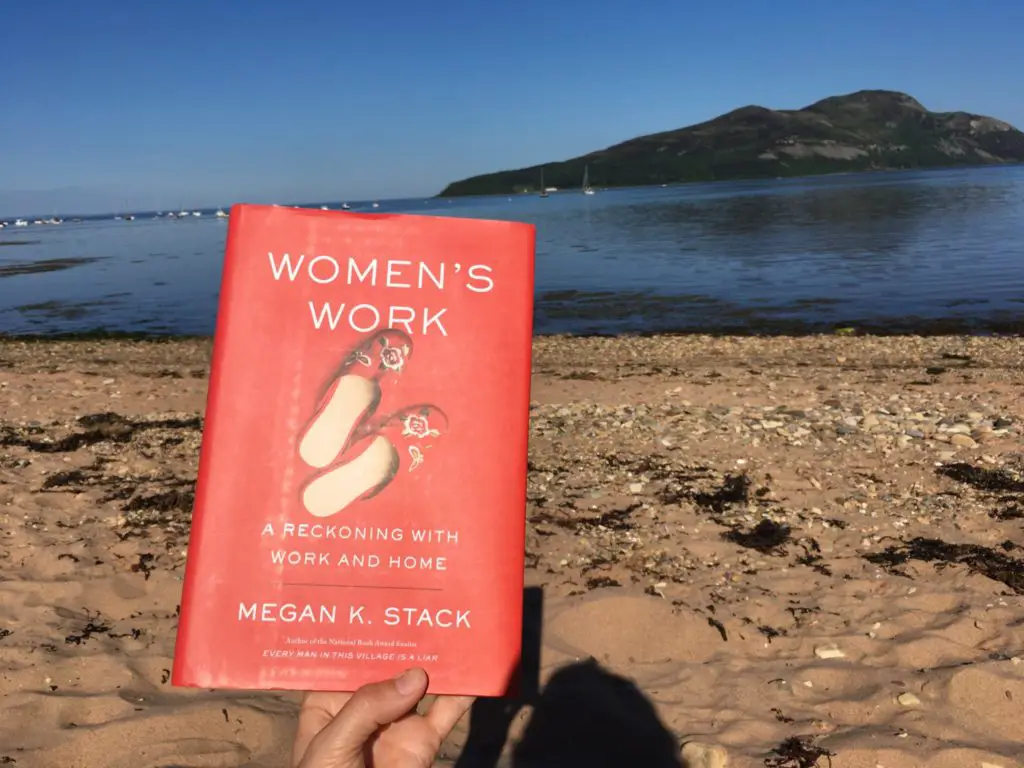 Women's Work, a book by Megan K Stack held up on a sunny day at the beach on Isle of Arran Scotland