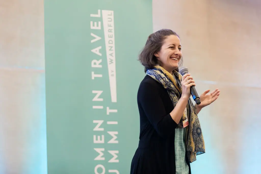 Amanda Walkins speaking on stage in front of a WITS travel conference banner