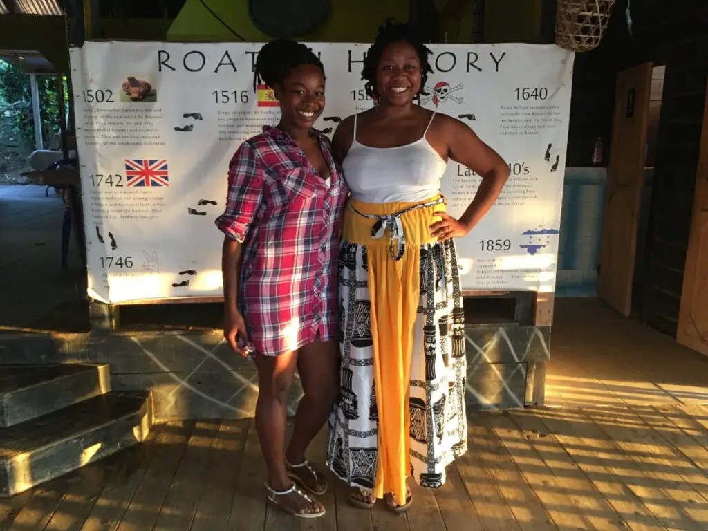 Nora and Audrey Flores of the Flamingo Cultural Center in Roatan standing in front of the history of Roatan timeline