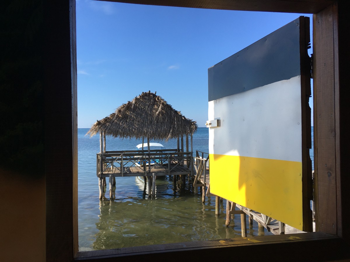 An open window at the Garifuna Cultural Center in Roatan overlooking the calm Caribbean Sea and a thatched palapa dock