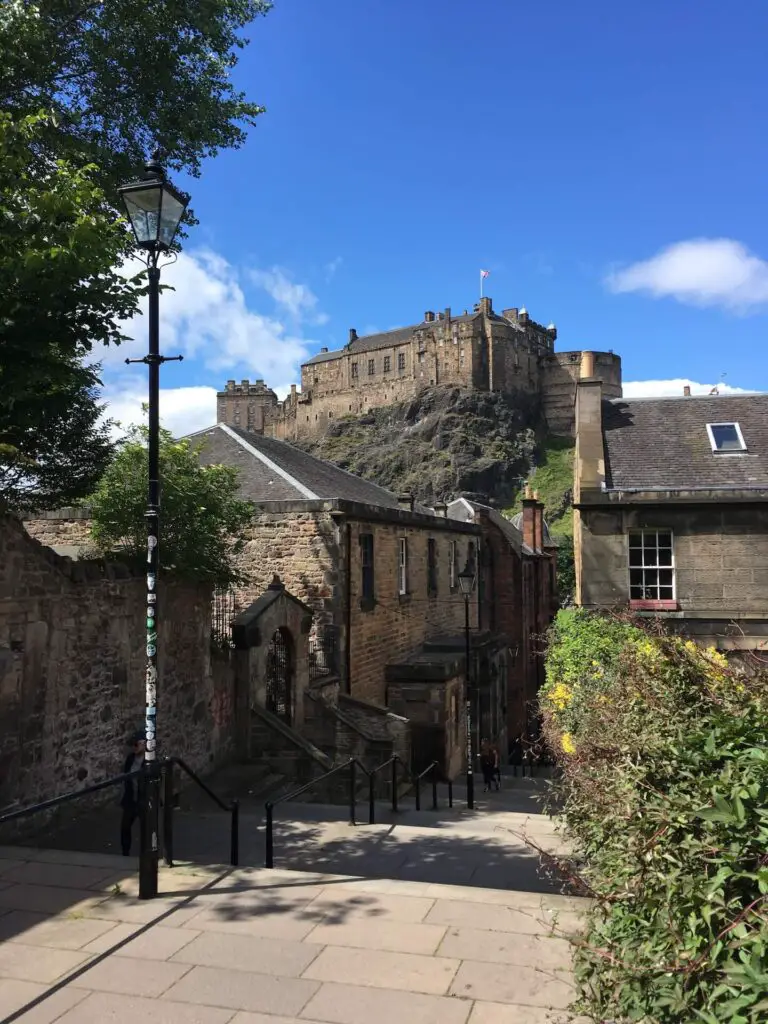 View of Edinburgh Castle from the stairs called The Vennel. A bright blue sky serves as a picture-perfect backdrop 